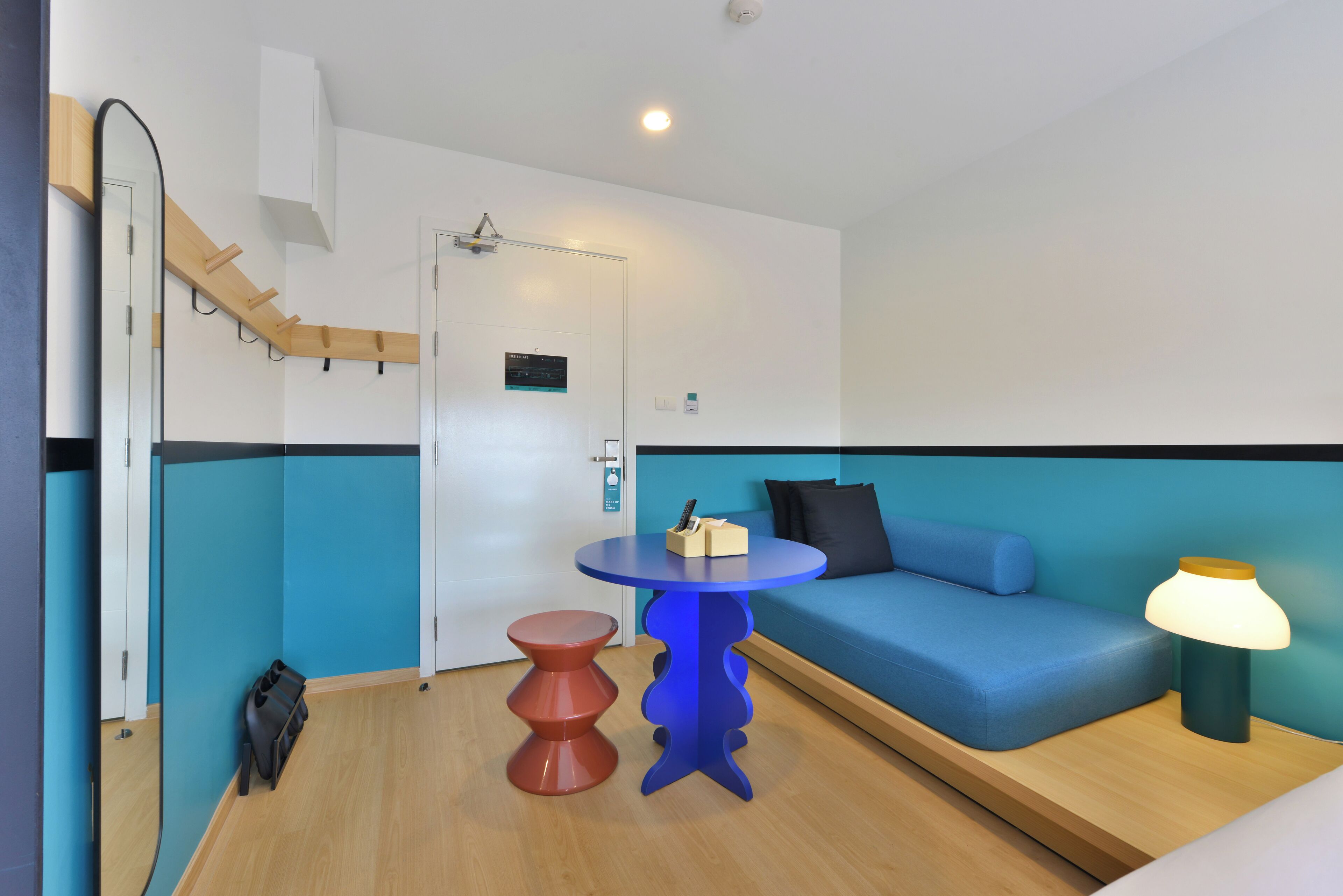 A modern room with a blue and white color scheme, a round table with a lamp, a blue sofa, and a wooden bench.
