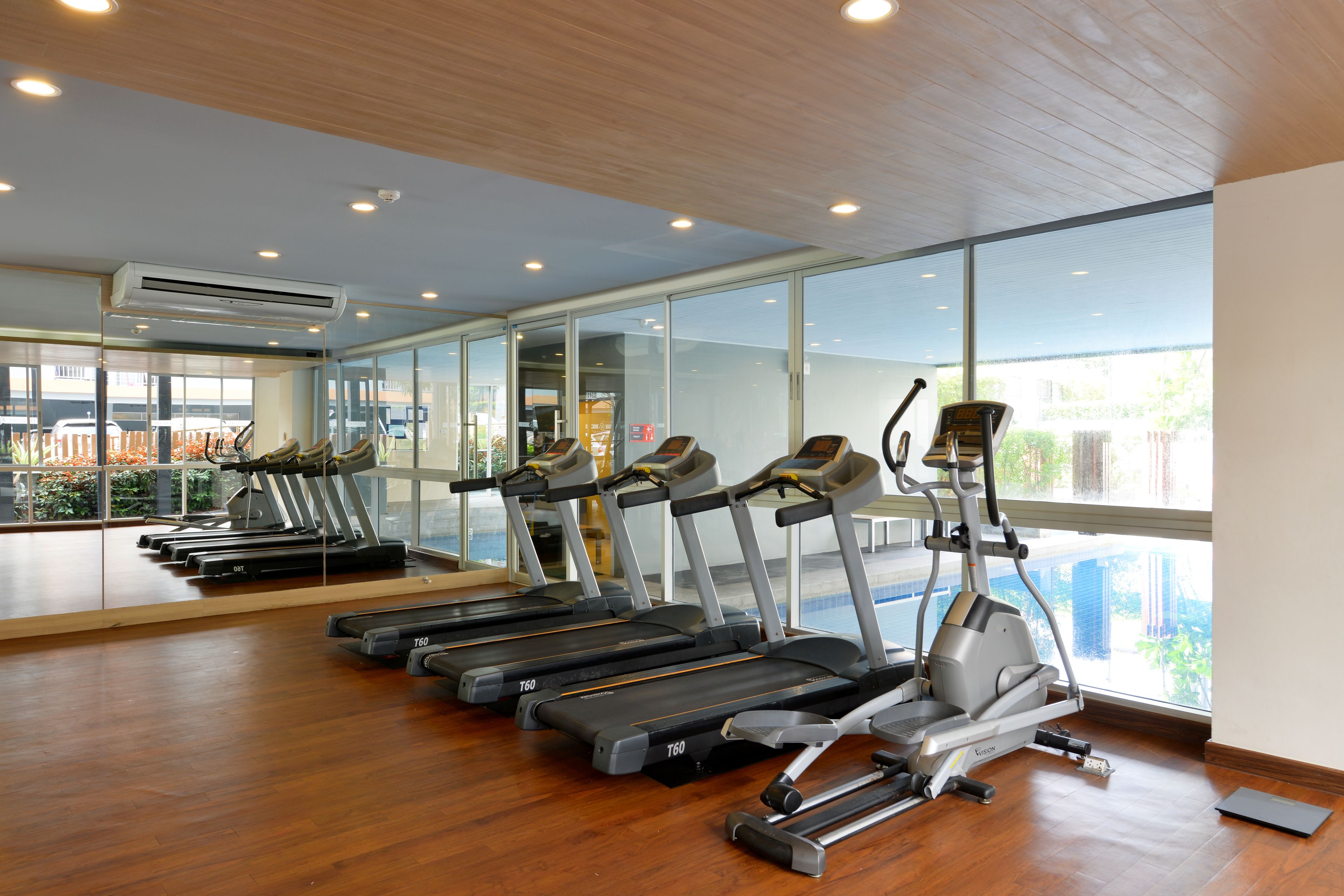 A gym with treadmills, elliptical machines, and a large mirror wall.