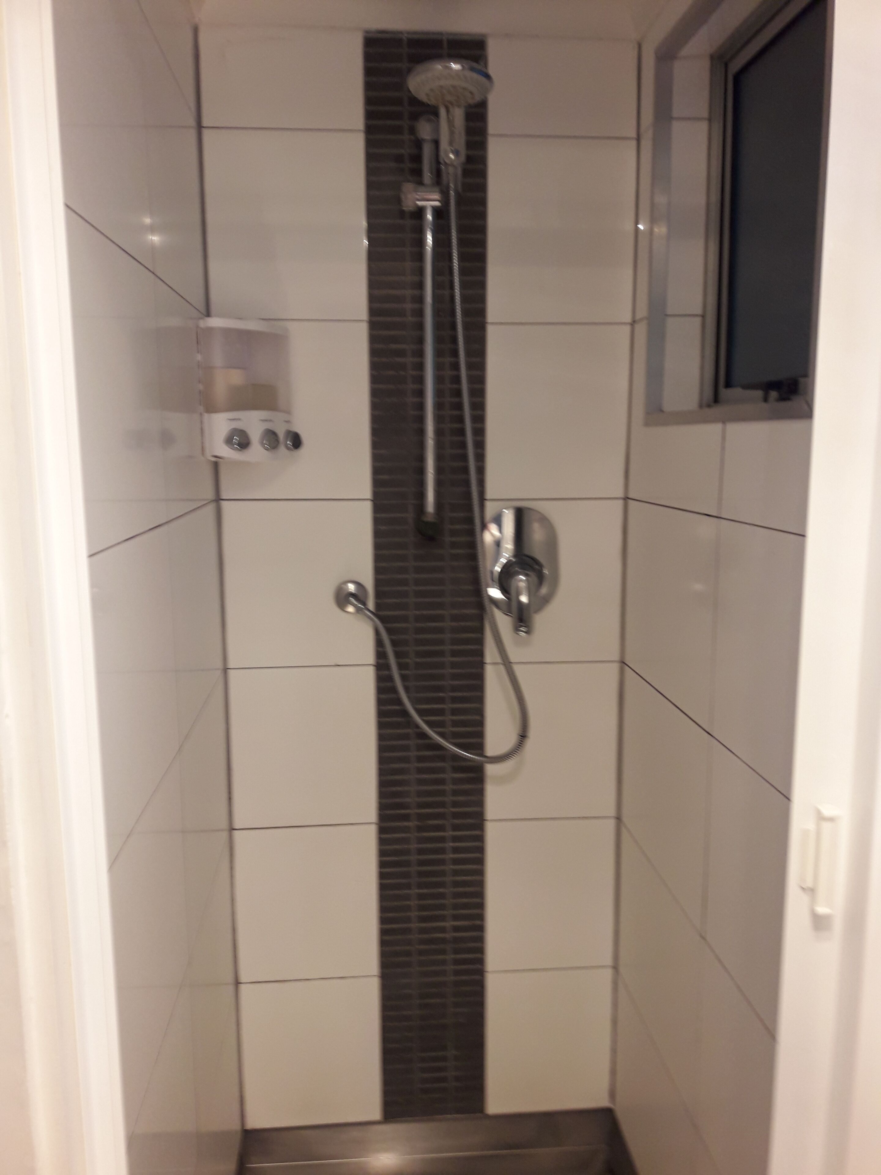 Une cabine de douche équipée d’un pommeau de douche à main, d’un robinet mural et d’un panneau de commande avec des boutons.