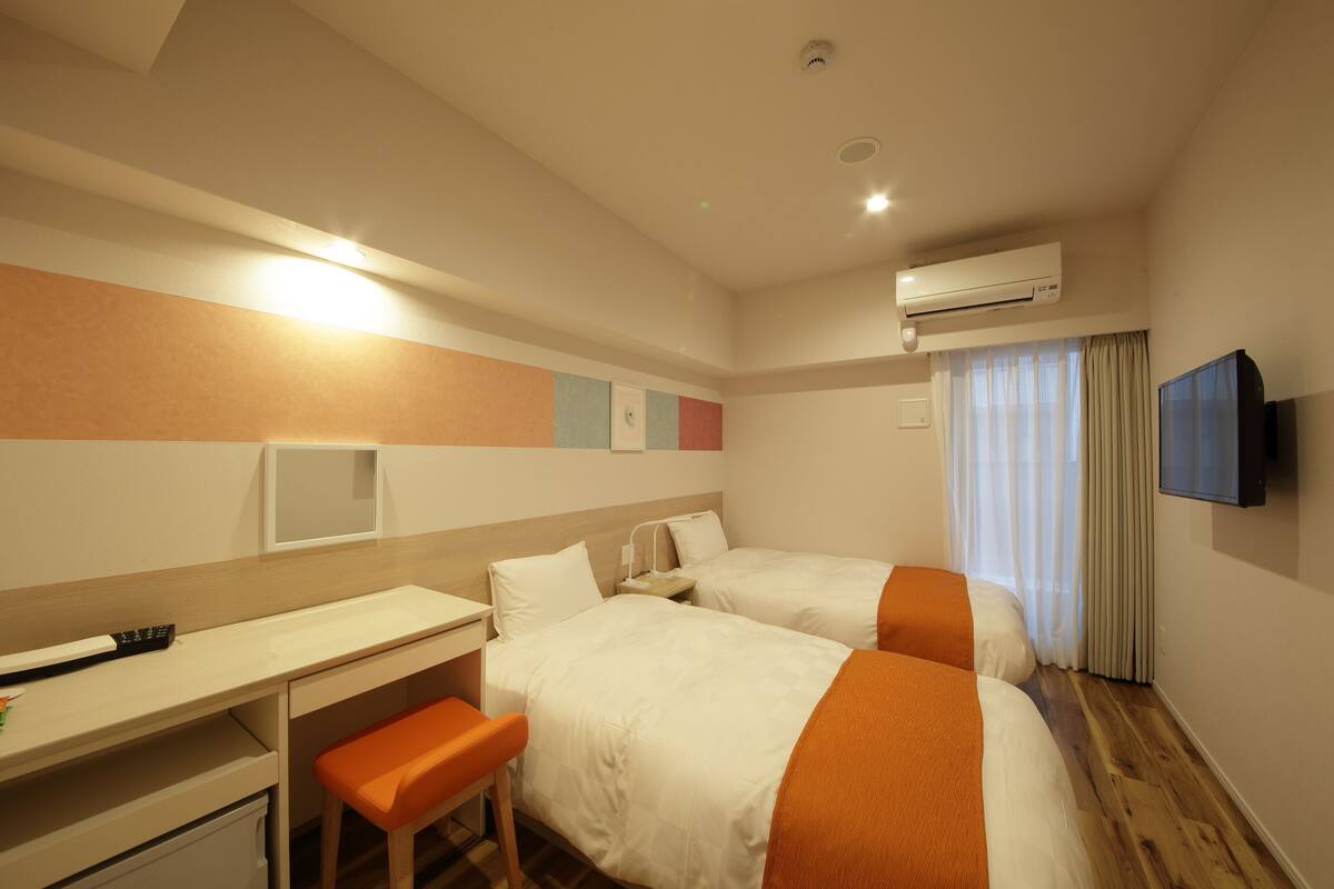 Ein Hotelzimmer mit zwei Betten, einem Schreibtisch, einem Stuhl, einer Klimaanlage und einem Fernseher.