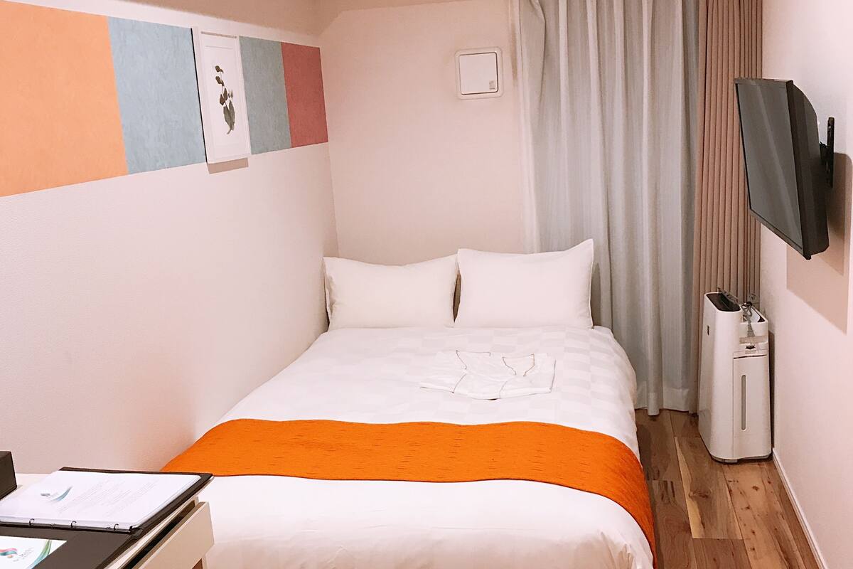 Ein Hotelzimmer mit einem Bett, einem Schreibtisch, einer Klimaanlage, einem Fernseher und einem Mülleimer.