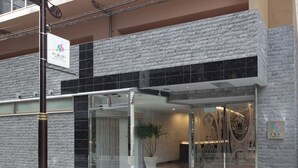 A modern hotel entrance with a stone facade, glass doors, and a potted plant. - SARASA HOTEL Shinsaibashi (Osaka)