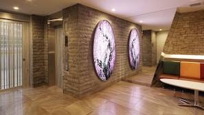 A modern lobby with a stone wall, two elevators, and a seating area with a colorful bench. - SARASA HOTEL Shinsaibashi (Osaka)