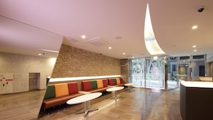A modern lobby with a stone wall, a reception desk, and a seating area with colorful cushions. - SARASA HOTEL Shinsaibashi (Osaka)