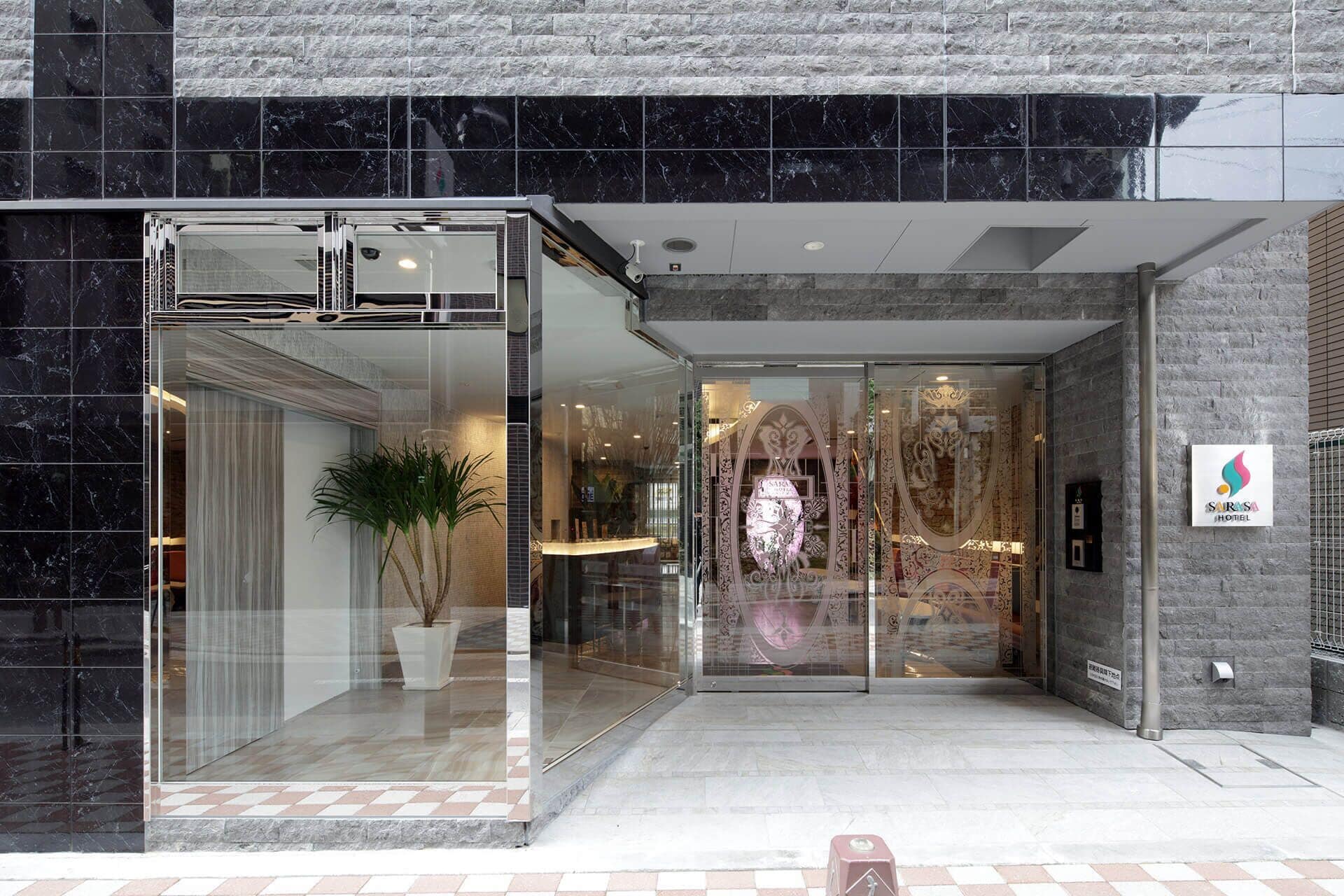 A hotel entrance with a glass door, a potted plant, and a sign for the Sarasa Hotel.