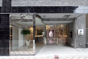 A hotel entrance with a glass door, a potted plant, and a sign for the Sarasa Hotel. - SARASA HOTEL Shinsaibashi (Osaka)