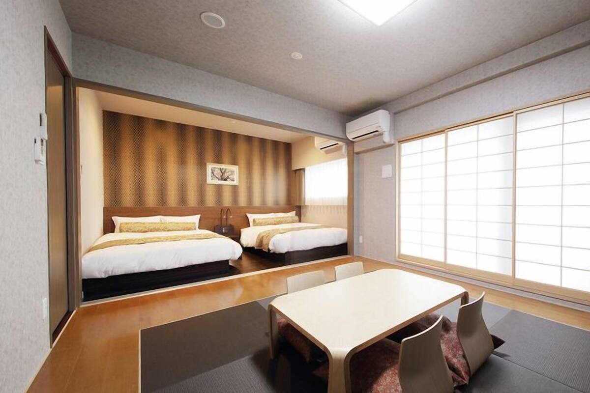 Ein Hotelzimmer mit zwei Betten, einem Esstisch und einem großen Fenster.