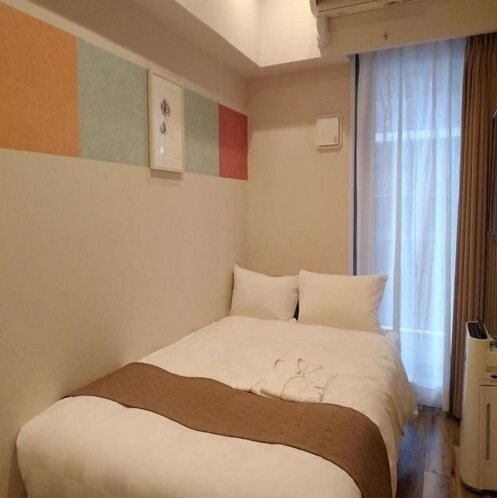 A hotel room with a bed, a window with curtains, and a wall with a picture.