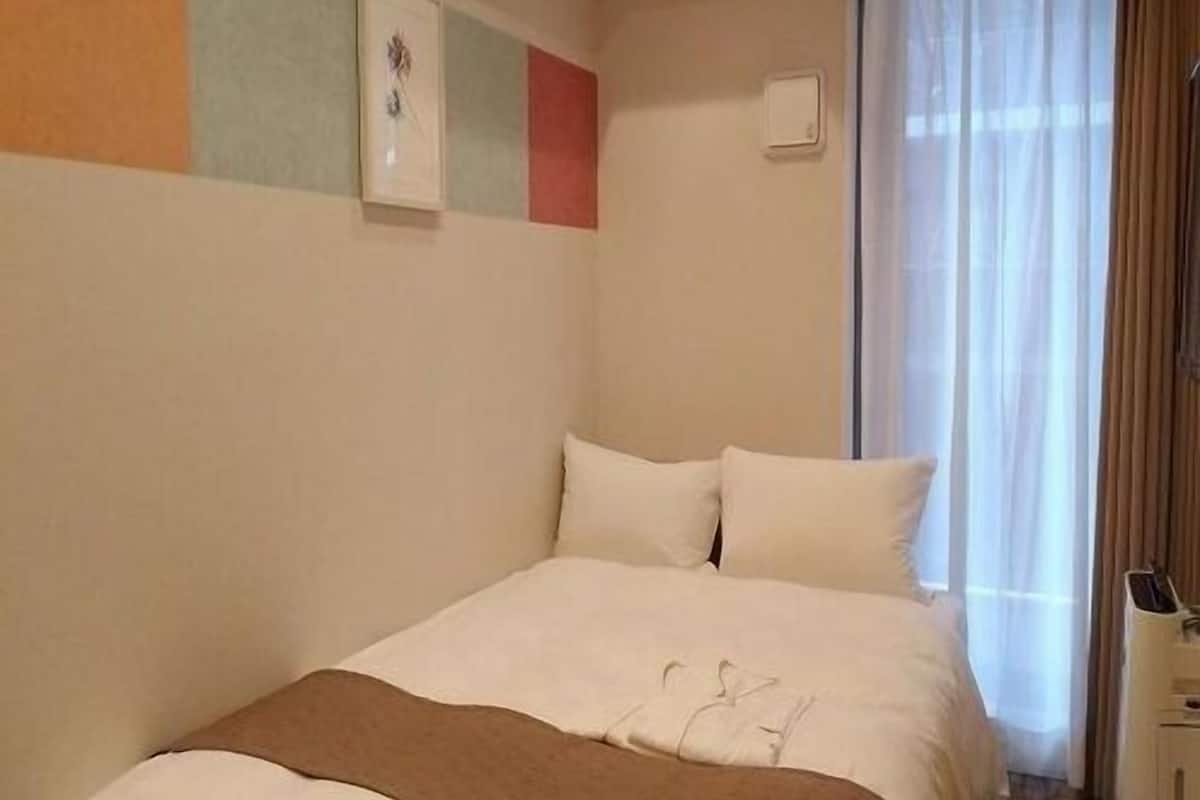 A hotel room with a bed, a window with curtains, and a wall with a picture.