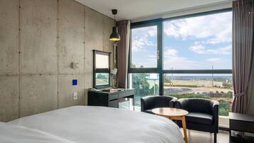 Quarto de hotel com uma cama grande, uma escrivaninha, uma cadeira e vista do horizonte através de grandes janelas.