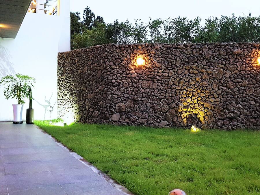 A stone wall with two lights, a potted plant, and a pathway.