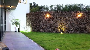 A stone wall with two lights, a potted plant, and a pathway. - CNB HOTEL (COZYANDBOUTIQUE) (Seogwipo)