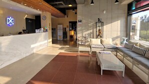 A hotel lobby with a reception desk, seating area, and a view of the outside. - CNB HOTEL (COZYANDBOUTIQUE) (Seogwipo)