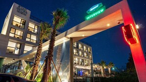 L’entrée d’un hôtel, avec une pancarte indiquant « ENTRETIEN », des palmiers et une façade de bâtiment moderne.