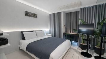 A modern hotel room with a neatly made bed, a desk with a chair, a flat-screen TV, and a potted plant.