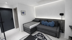 A modern bedroom with a grey sofa bed, a black and white rug, a black floor lamp, and a framed picture on the wall. - JEJU DSPHERE HOTEL (Jeju City)