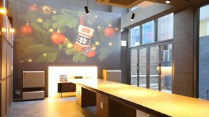 A modern hotel lobby with a long reception desk, a large digital Christmas display, and large windows providing a view of the outside. - JEJU DSPHERE HOTEL (Jeju City)