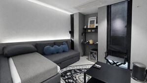 A modern, compact living space with a grey sofa, a small table, and a black trash bin. - JEJU DSPHERE HOTEL (Jeju City)