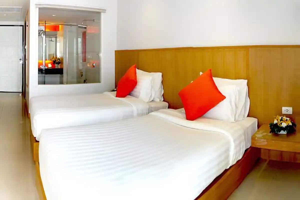 Une chambre d’hôtel avec deux lits, chacun agrémenté de draps blancs et d’oreillers rouges, d’une tête de lit en bois et d’une petite table sur laquelle est posé un vase de fleurs.