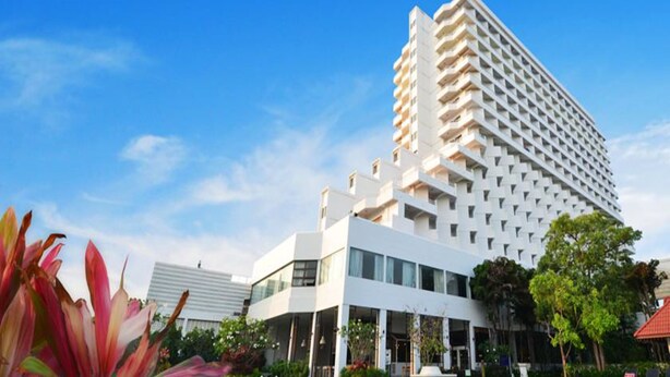 Een modern hotel met een opvallende witte gevel, meerdere balkons en een helderblauwe lucht.