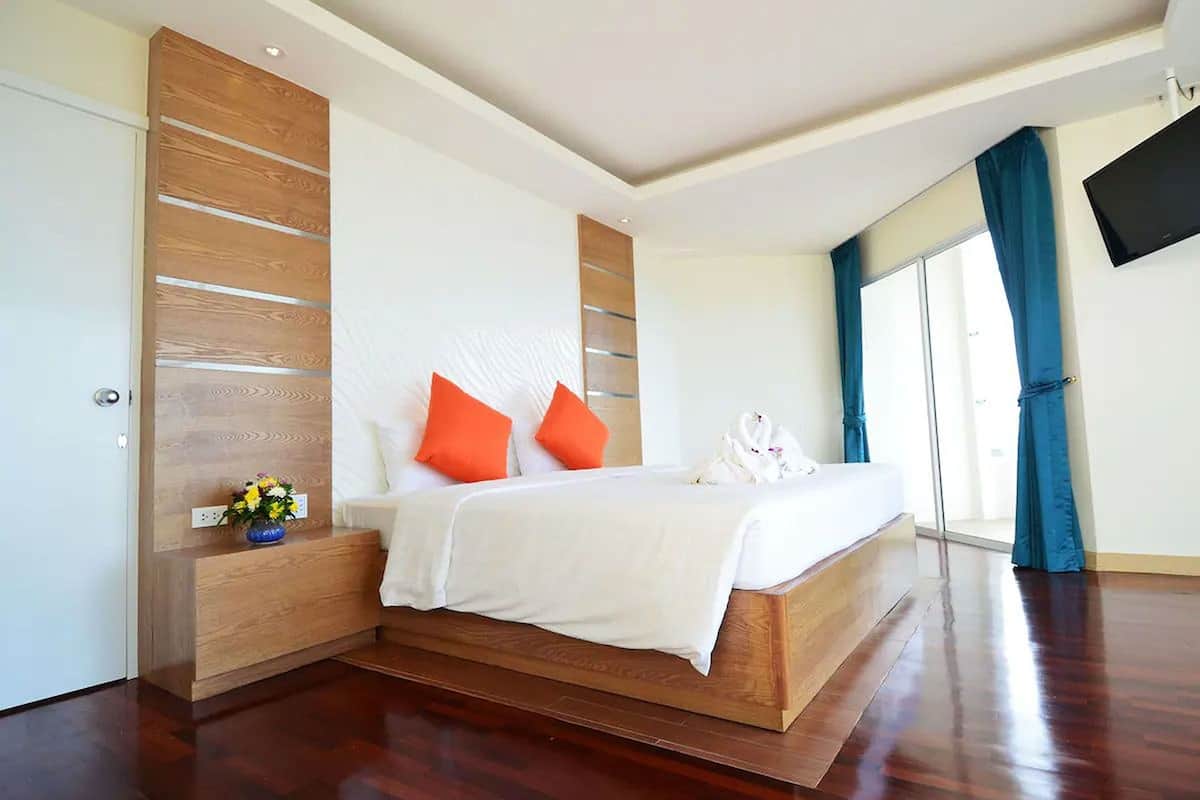 Une chambre moderne avec un grand lit, une tête de lit en bois et un téléviseur à écran plat fixé au mur.