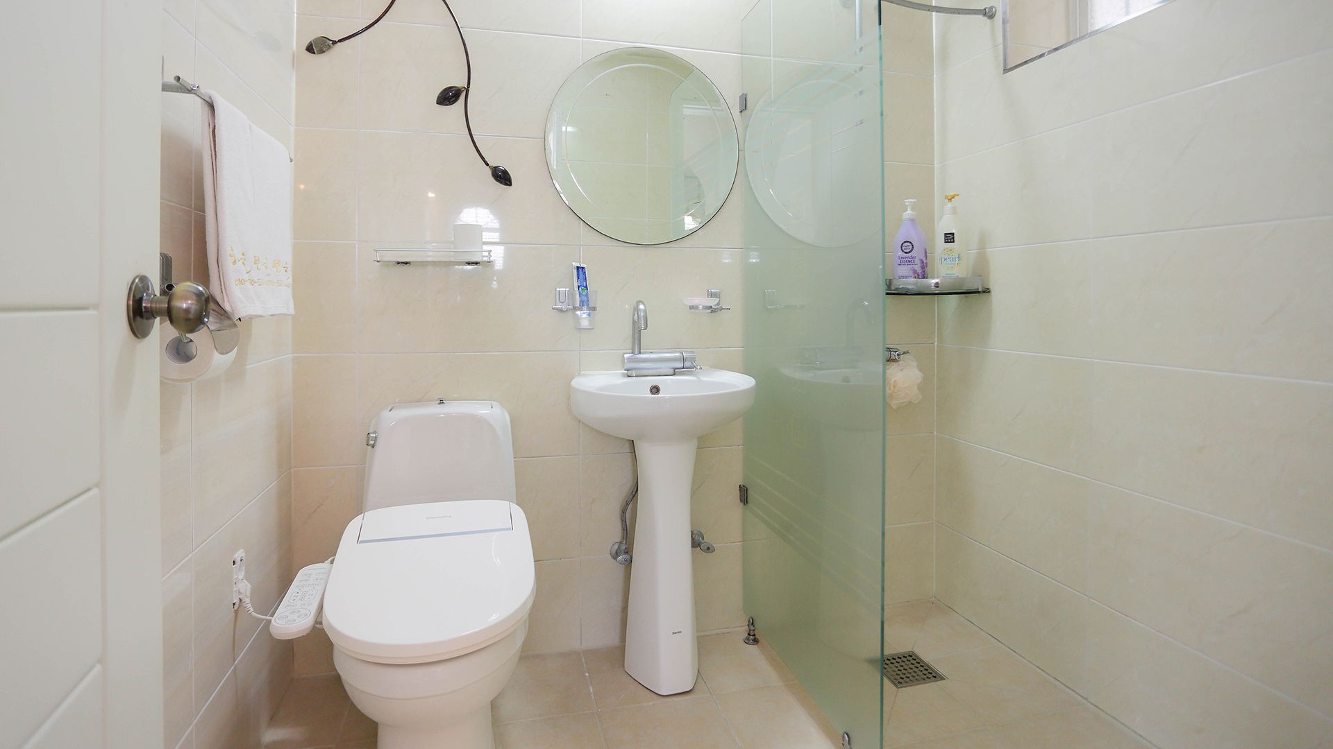 A modern bathroom with a toilet, a pedestal sink, a glass shower enclosure, and a round mirror.