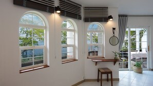 Una habitació amb grans finestres d'arc, una banca de fusta, un tamboret petit, un mirall i una planta en test.