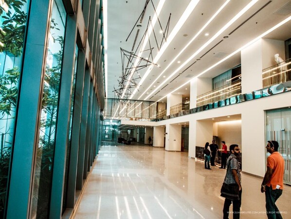 Un hall amplio y moderno con techo alto, pisos reflectantes y una combinación de barandillas de vidrio y metal.