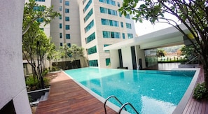 A modern swimming pool with a wooden deck, surrounded by tall buildings and greenery. - Summer Suites Vacation Home (Kuala Lumpur)