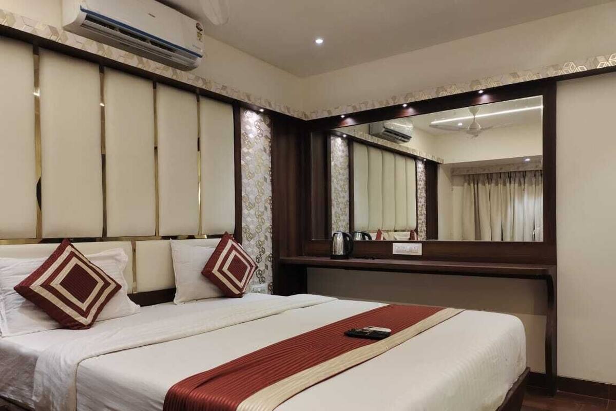 Ein Hotelzimmer mit einem großen Bett, einem Nachttisch mit Lampe, einem Spiegel und einer Klimaanlage.