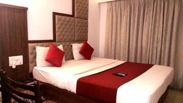 Habitación de hotel con una cama grande, cabecera de madera, manta roja y un control remoto sobre la cama.
