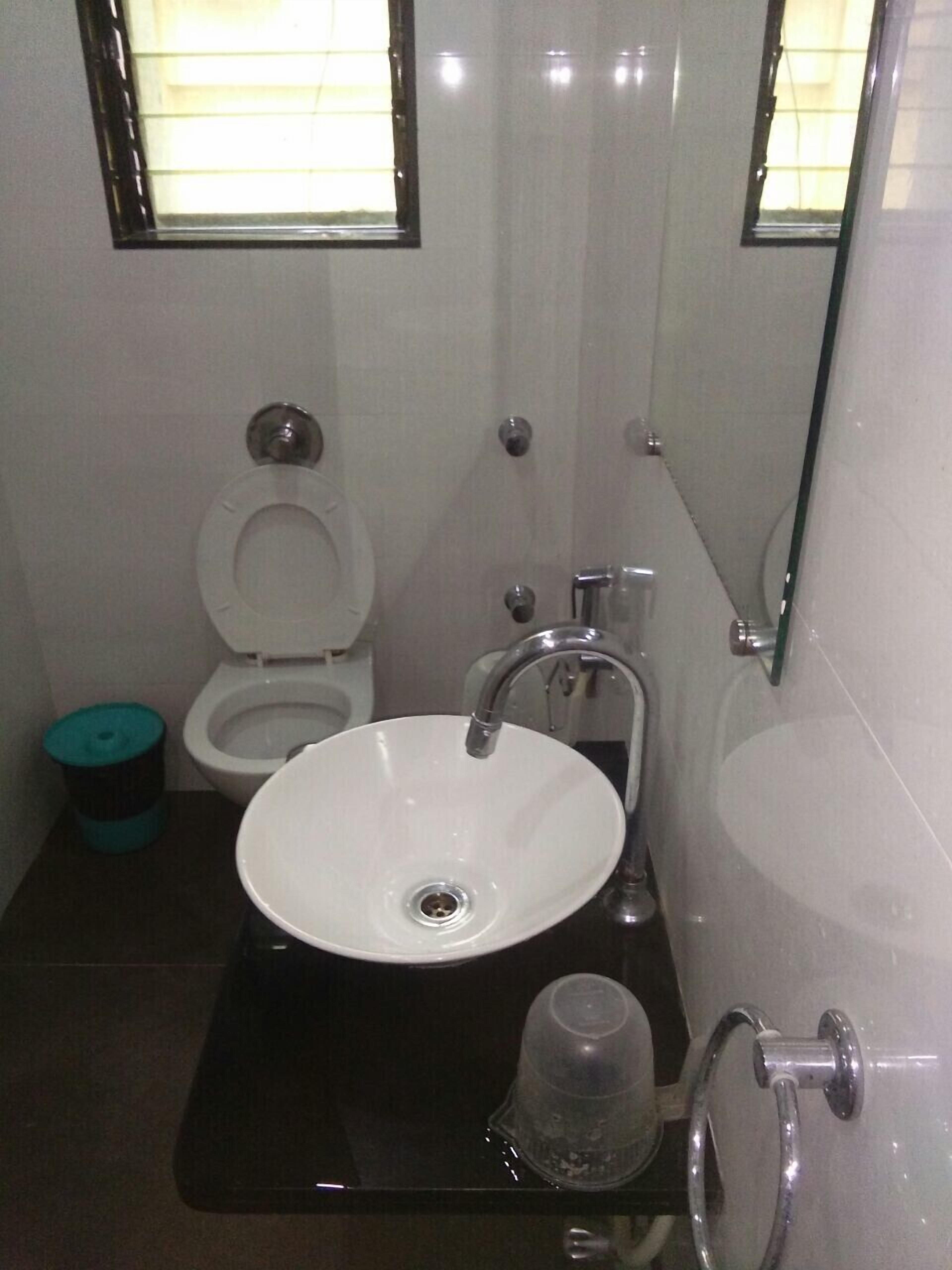 A bathroom with a white toilet, a sink with a mirror above it, and a trash bin.