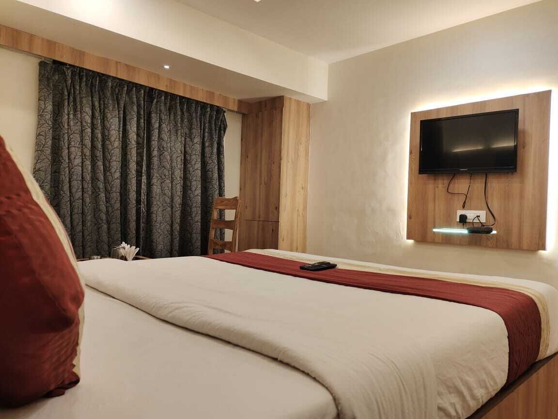 A hotel room with a large bed, a TV mounted on the wall, and a wooden headboard.