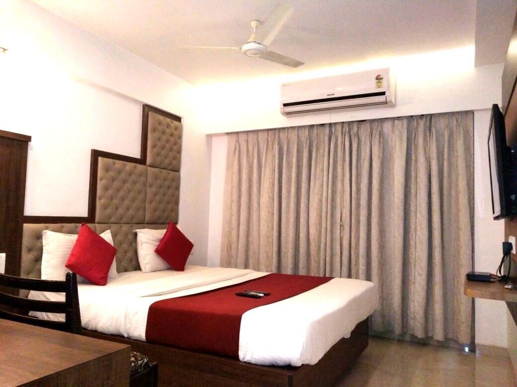 Une chambre d’hôtel équipée d’un lit, d’un ventilateur de plafond, d’un climatiseur, d’une télévision et d’une fenêtre avec des rideaux.