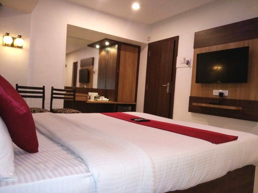 A hotel room with a bed, a TV mounted on the wall, a wooden wardrobe, and a mirror.