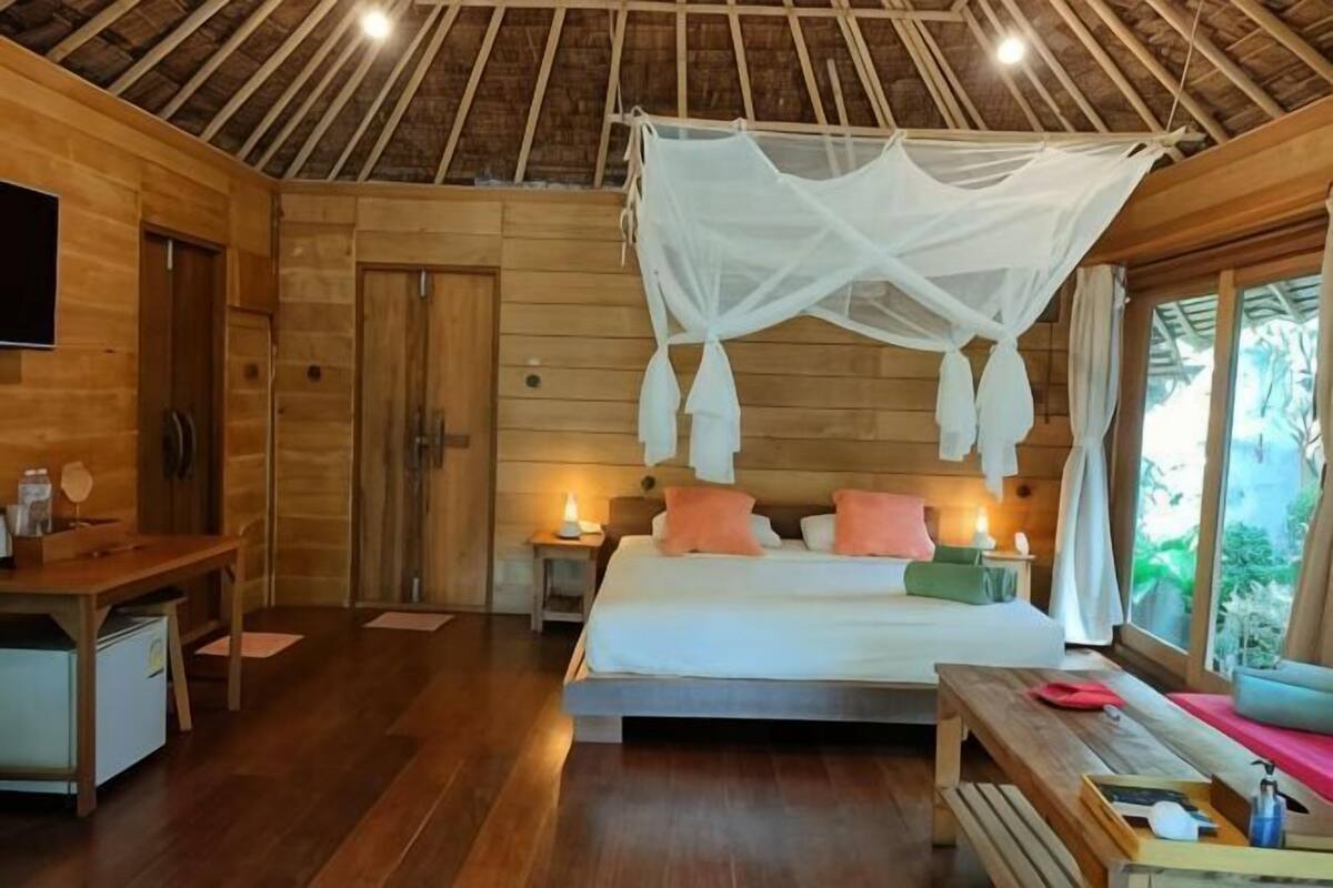 Una habitación de madera con una cama, mesitas de noche, un banco y un televisor.