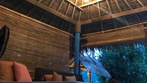 Un espacio de estar al aire libre cubierto, con techo de paja y paredes de bambú.