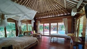 Una habitación amplia con una cama grande, un escritorio de madera y un banco. Hay un ventanal con vistas al exterior.