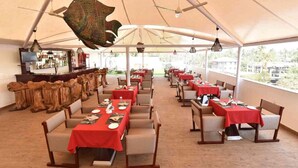 Ein Restaurant mit mehreren Tischen, die mit roten Tischdecken bedeckt sind, Holzstühlen und hängenden Pendelleuchten.