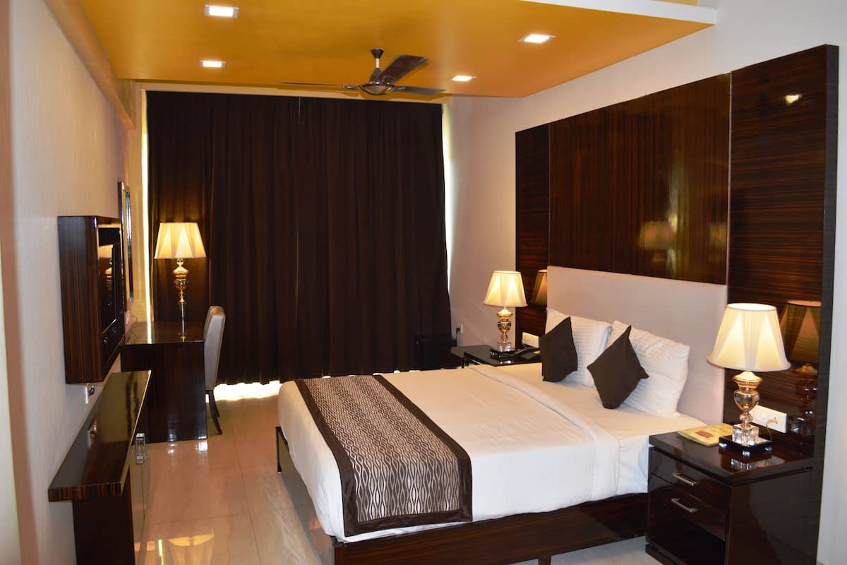 Habitación de hotel con una cama grande, dos mesitas de noche con lámparas, un televisor de pantalla plana, un ventilador de techo y paneles de madera oscura en las paredes.