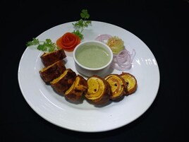A plate with sliced meat, a bowl of green sauce, and garnishes.