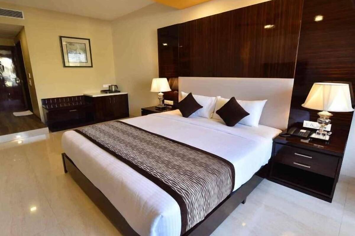 Habitación de hotel con una cama grande, mesitas de noche, un cabecero de madera y un cuadro enmarcado en la pared.