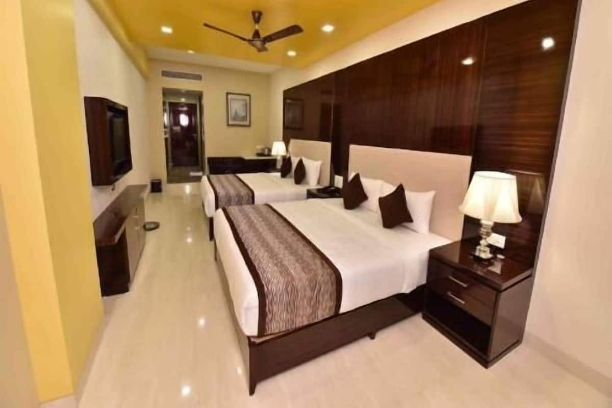 Habitación de hotel con dos camas, un ventilador de techo, un televisor y una mesita de noche con lámpara.