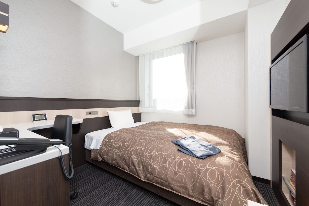 A hotel room with a bed, desk, chair, and a television.