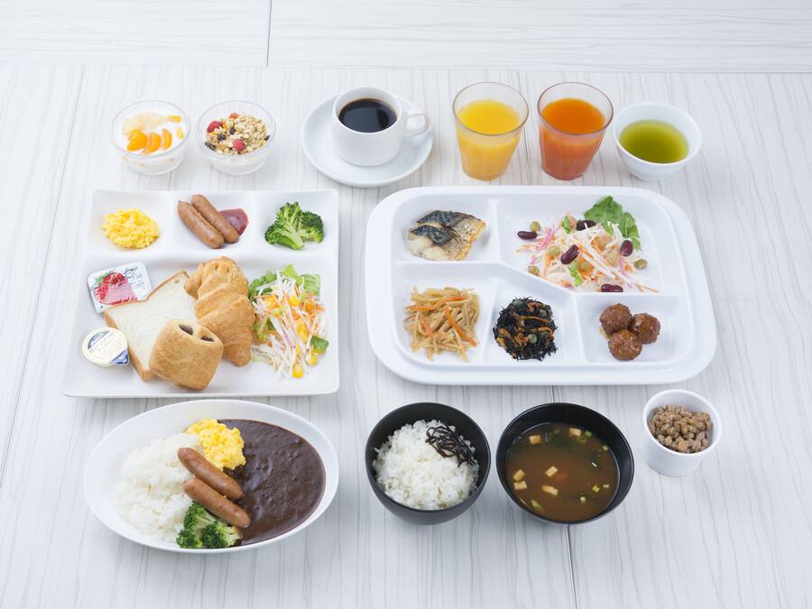 Un assortiment de plats pour le petit-déjeuner, notamment des œufs, des saucisses et du riz, servis dans des assiettes et des bols blancs.