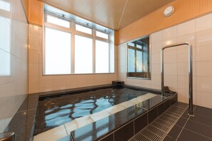 Una piscina interior moderna con paredes de vidrio transparente, una escalera metálica y suelo de baldosas.