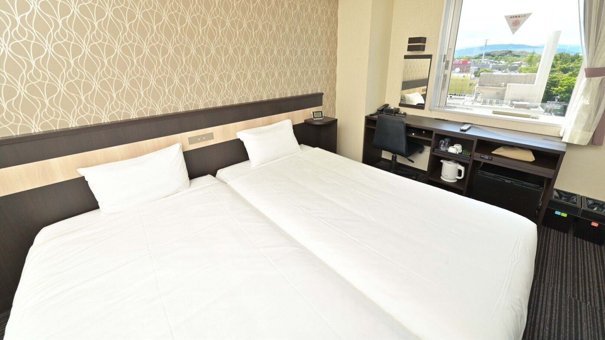 Habitación de hotel con una cama grande, mesitas de noche, un escritorio con silla, un espejo y una ventana con vistas.