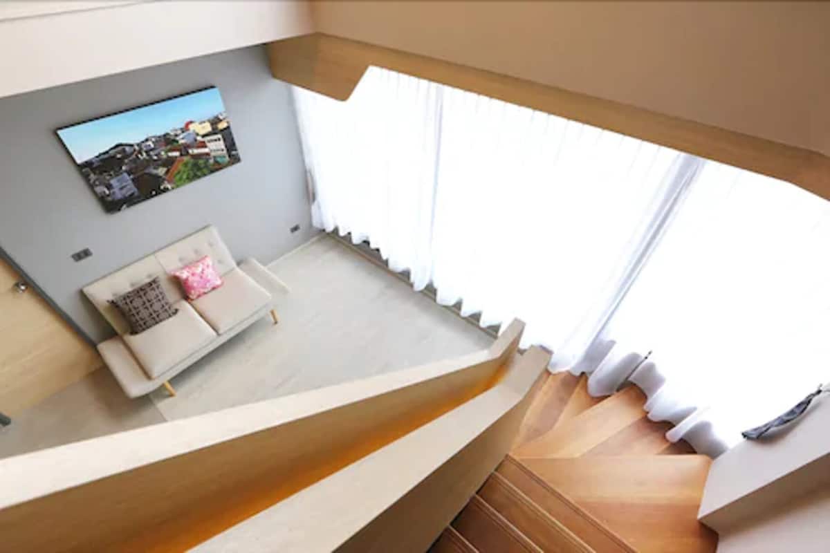 A modern living room with a sofa, a wall-mounted picture, and a staircase leading to an upper level.
