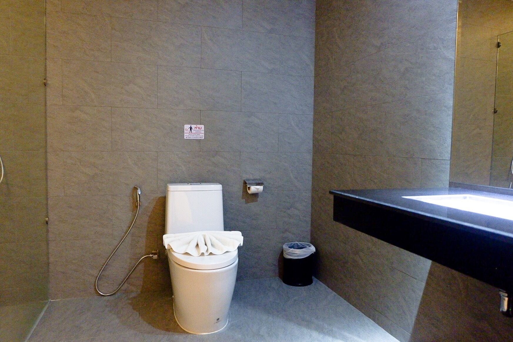 Un baño con inodoro, un bote de basura, dispensador de toallas de papel y lavamanos.