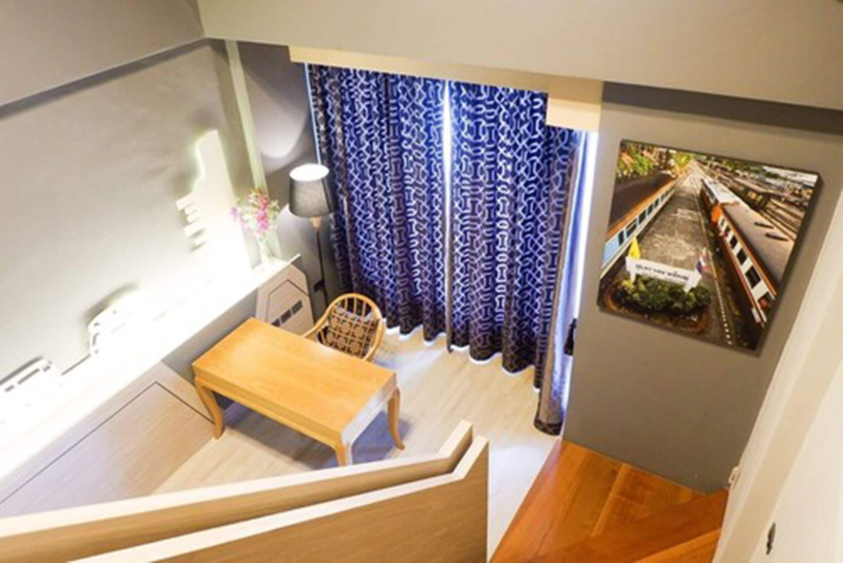 A room with a wooden desk, a chair, a lamp, and a window with patterned curtains.